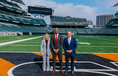 Bengals Chief Partnership Officer Lacy Ekert, Ande Durojaiye, Miami’s vice president for strategy and partnerships, and President Greg Crawford standing on the Bengals field with a Miami University logo on a screen behind them