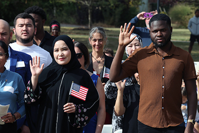 multiple people standing with their right hands up and some with flags in their hands during a Naturalization Ceremony