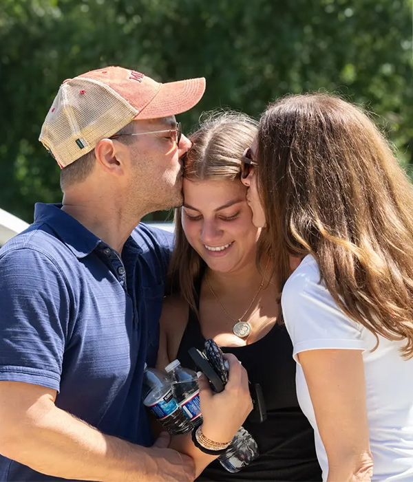a mother and father giving their daughter a kiss on either side of her head