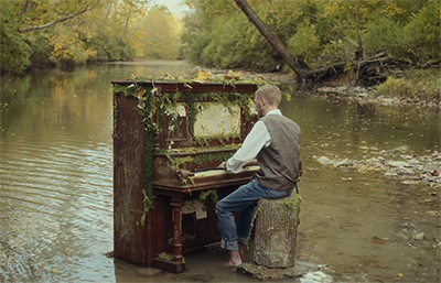 man playing on a moss covered piano in a creek