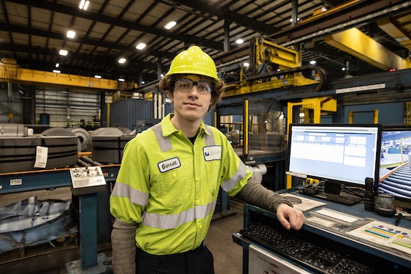 Work+ student on the job wearing a hard hat, protective goggles, and safety vest.