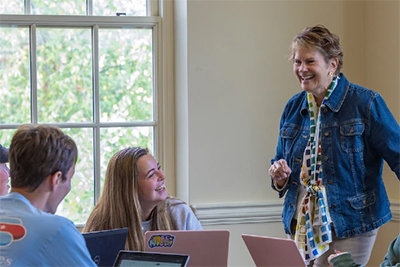 A smiling instructor engages with students in a classroom setting, fostering a lively discussion.