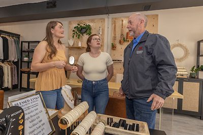 Three individuals engage in conversation at a boutique showcasing jewelry and accessories.