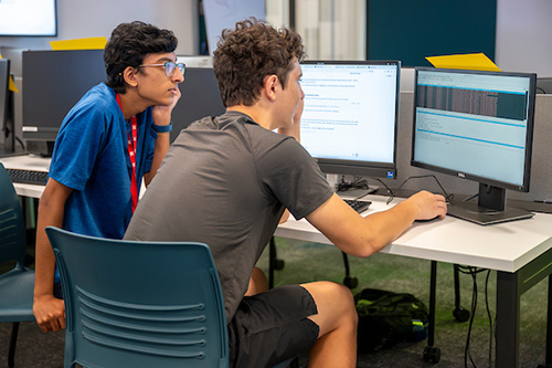 Two students focus on coding tasks at computers in a collaborative learning environment.