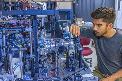 A researcher working carefully on a complex scientific apparatus surrounded by wires and equipment.
