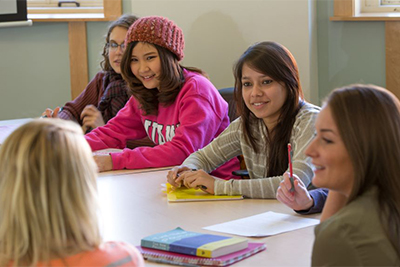 A group of diverse students engaged in a discussion around a table in a classroom setting.
