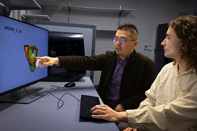 Two researchers discussing a computer model displayed on a monitor, with one pointing at the screen.