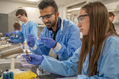Students engaged in a laboratory experiment, wearing protective gear and handling scientific equipment.