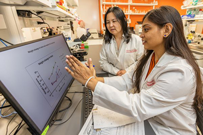 Two scientists collaborate in a laboratory setting, analyzing data displayed on a computer screen.