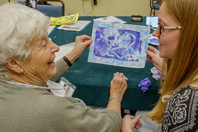 Two women engaged in a creative activity, sharing a colorful artwork during a workshop.