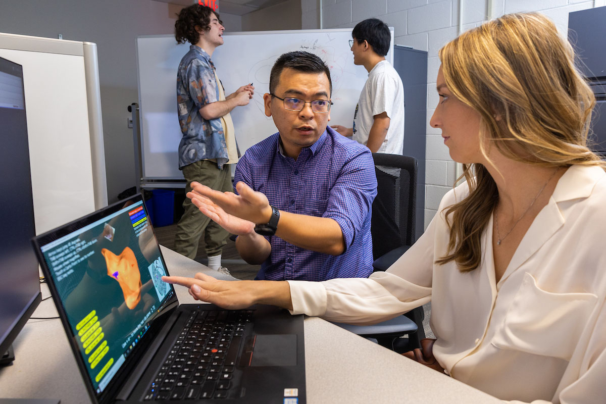 A student and professor collaborate over a laptop computer