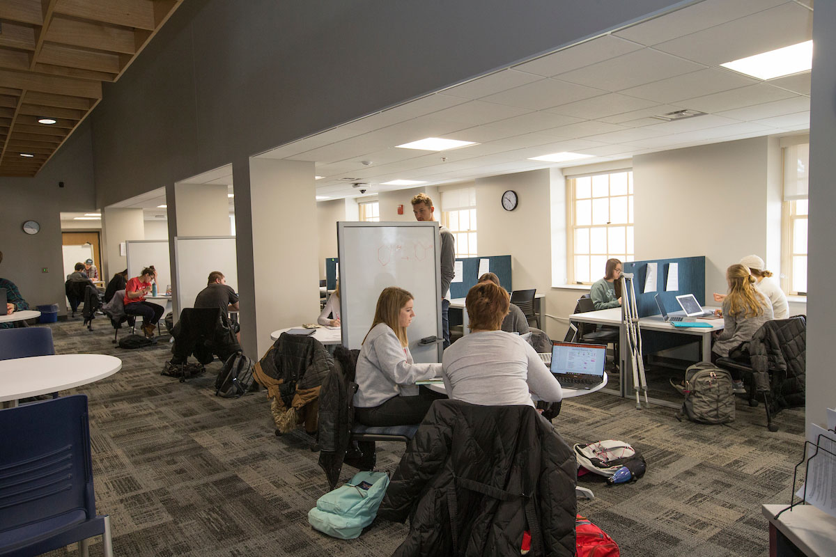 Students working with advisors at several tables in a large room