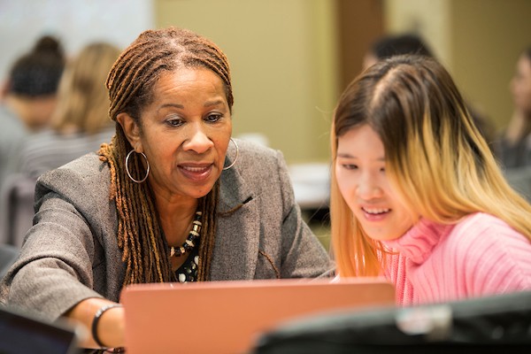 Professor Paula Saine works closely with a student in her class as they look at a laptop together