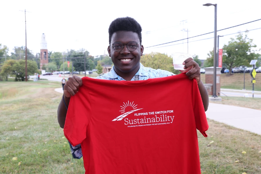 Student holding up a red shirt with the words "Flipping the switch for sustainability" written in white.