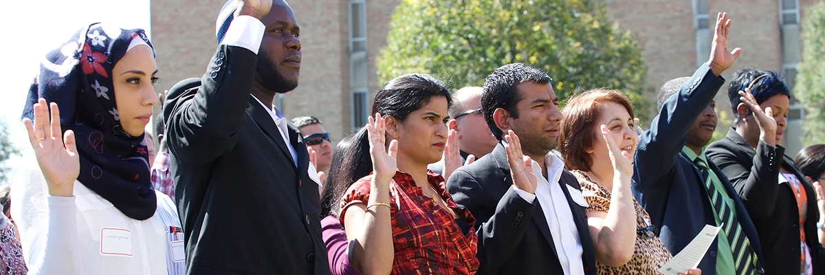 Multiple people lined up with their hands up at a naturalization ceremony