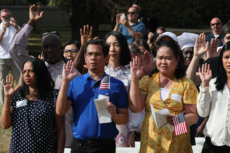 Group of citizens taking pledge, holding booklets and American flags.