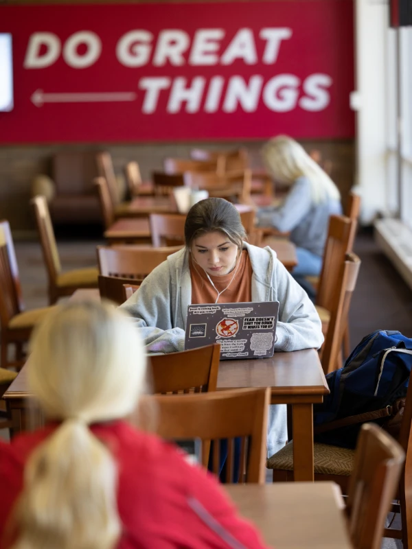 student working on her laptop with a sign behind her reading do great things
