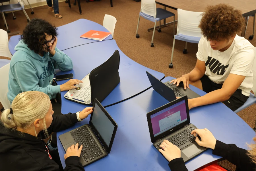 students working on their laptops at a large table