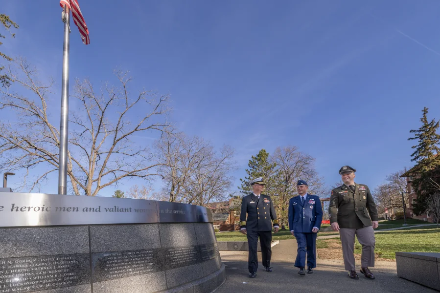 Three soldiers walking in their dress uniforms near the Veterans memorial