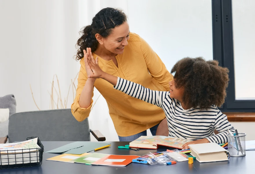Teacher and student high-fiving sitting at a table.