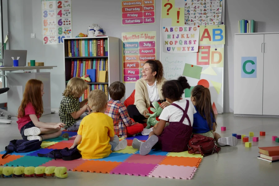 Teacher in classroom with small children sitting on a alphabet mat.