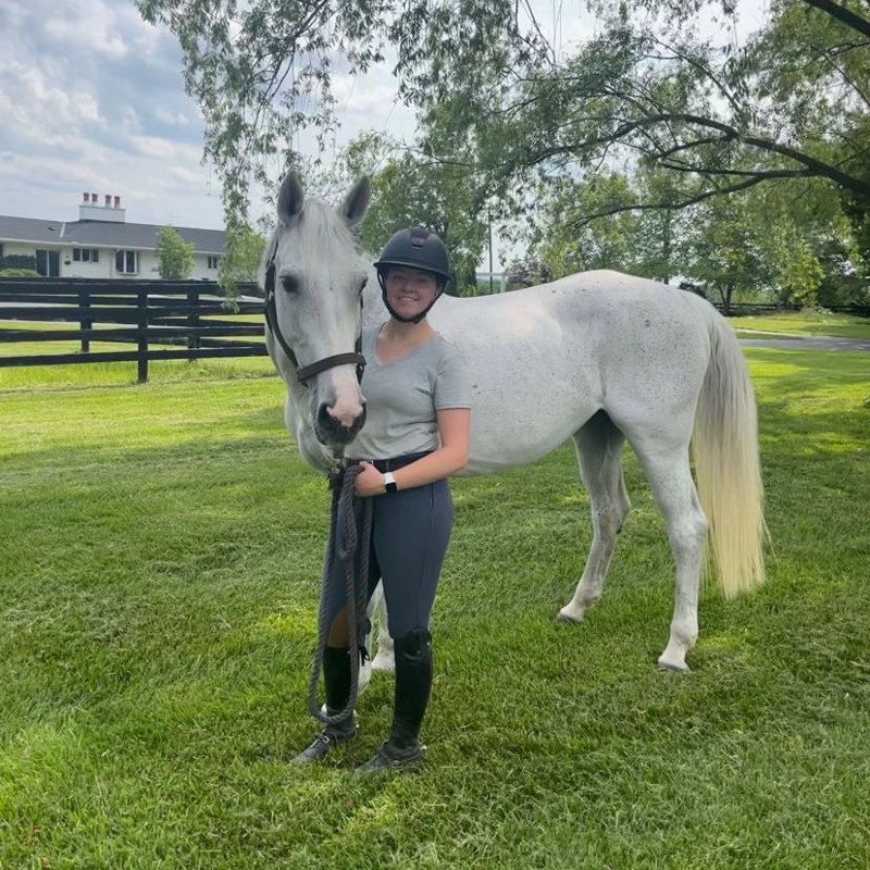 Anna Wilson standing next to her horse in a vibrant green pasture