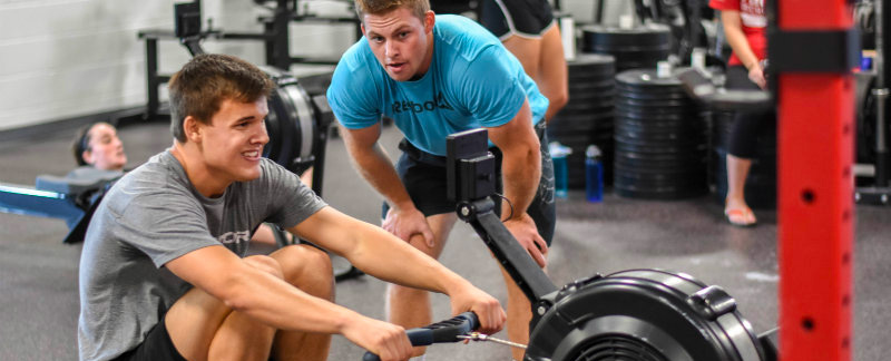 A Miami student using a rowing machine while a personal trainer looks on giving advice