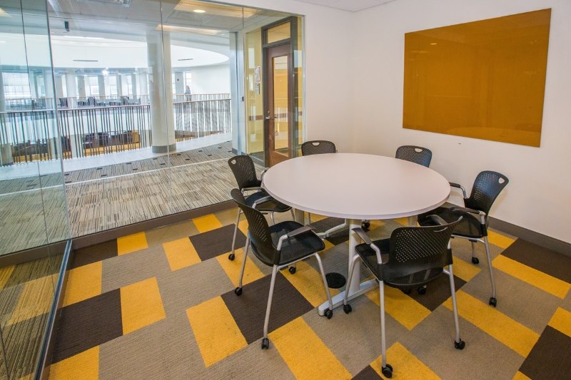 small room with a round table and six chair surrounding the table. Dry erase board on the wall. 