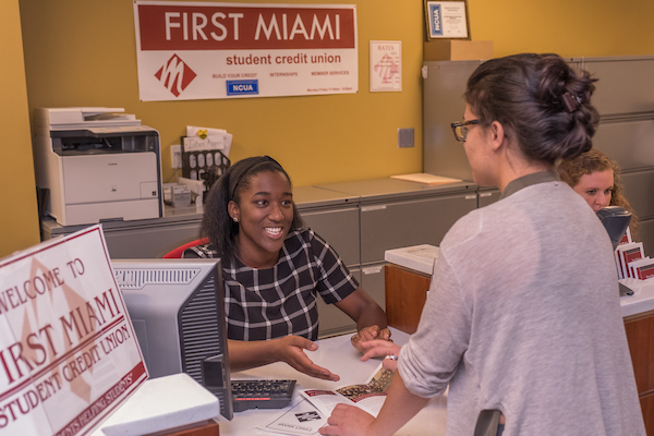 student serving a customer through a teller window 