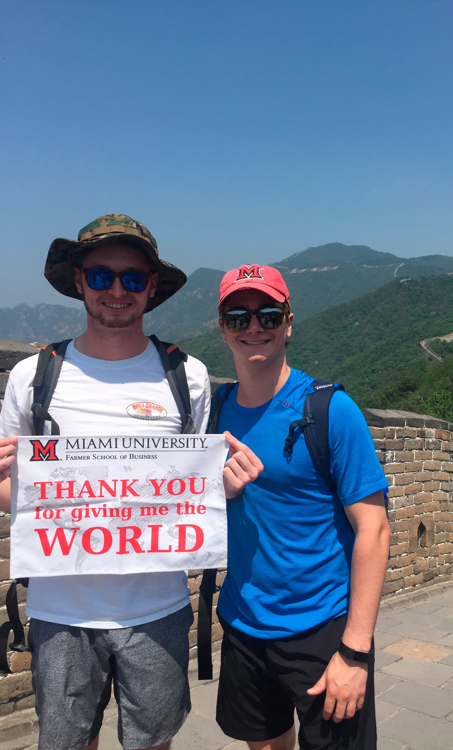 Two students pose in a mountain range with a sign reading "Miami University: you gave me the world."