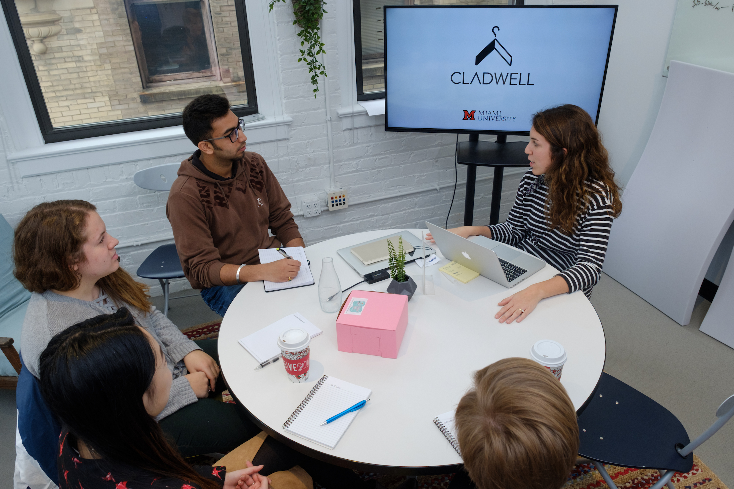 Four interns sit around a table with their supervisor to review a PowerPoint.