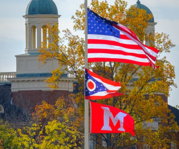 An American, an Ohio, and a Miami University flag fly in the wind in front of the Bell Tower.