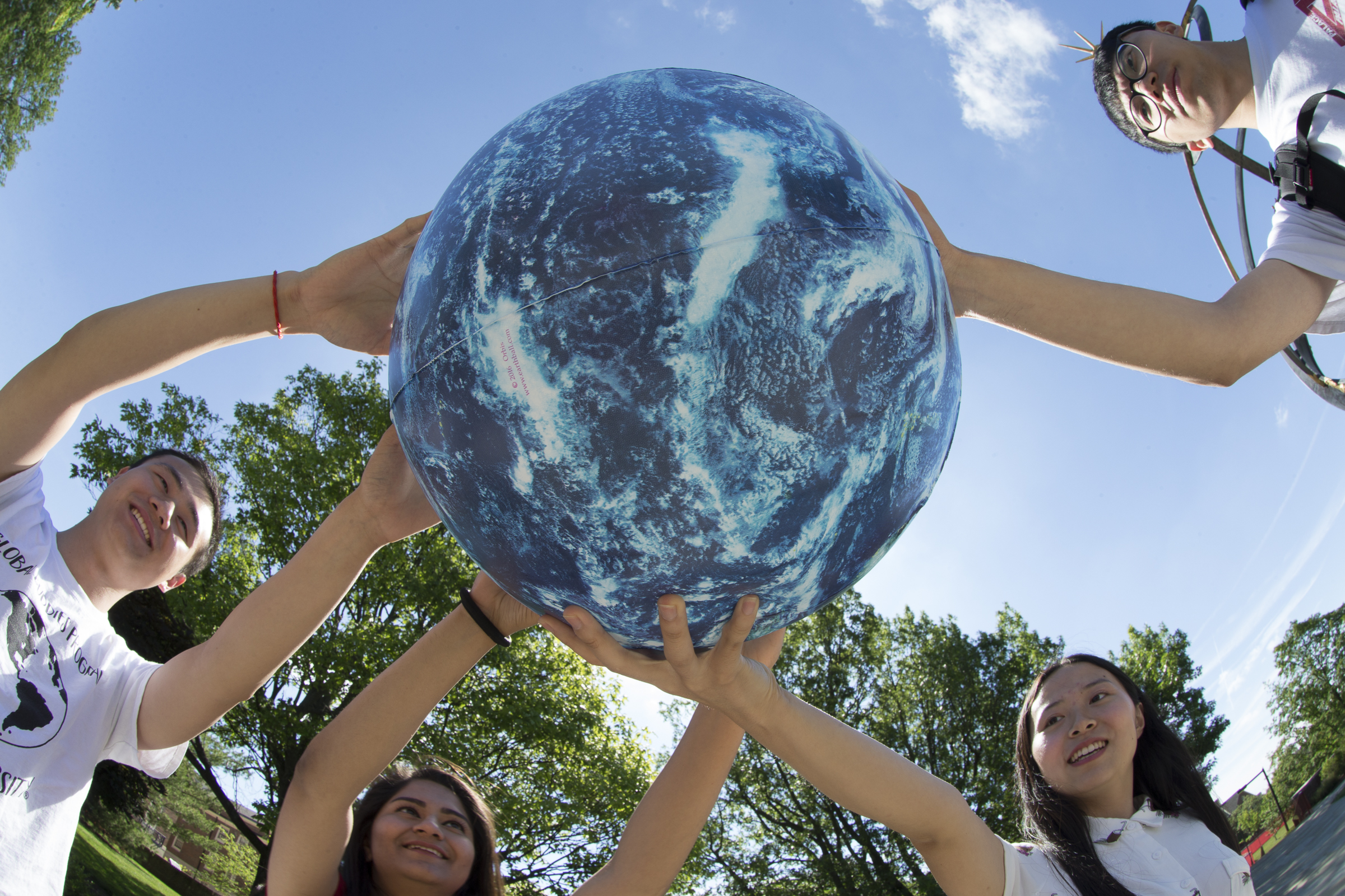 A group of four students hold up a globe together.