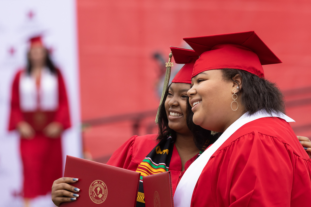 Two graduates smile while taking a picture at a commencement ceremony.