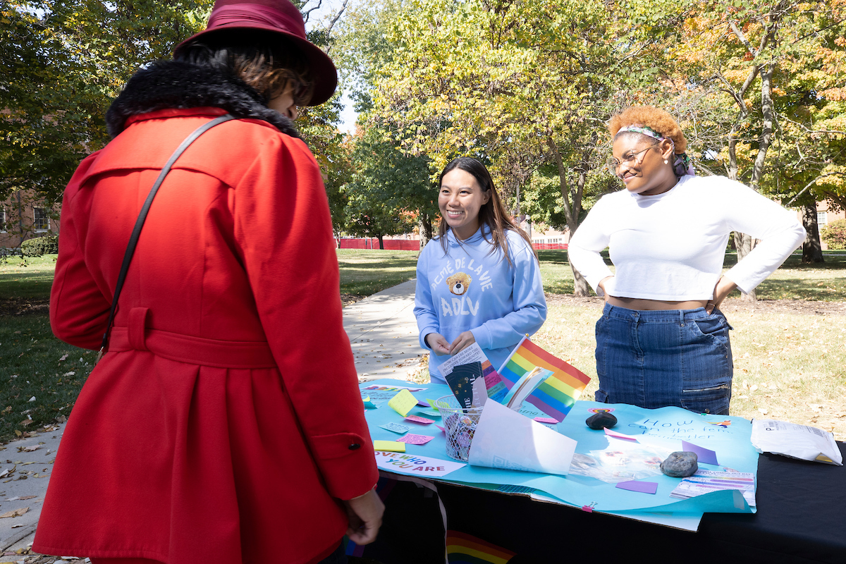 Three students talk around a table at Miami's National Coming Out Day event.