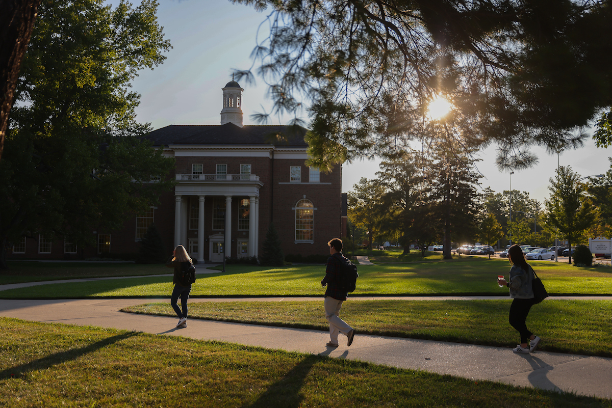 Students walk to class through the quad with the sun shining overhead.