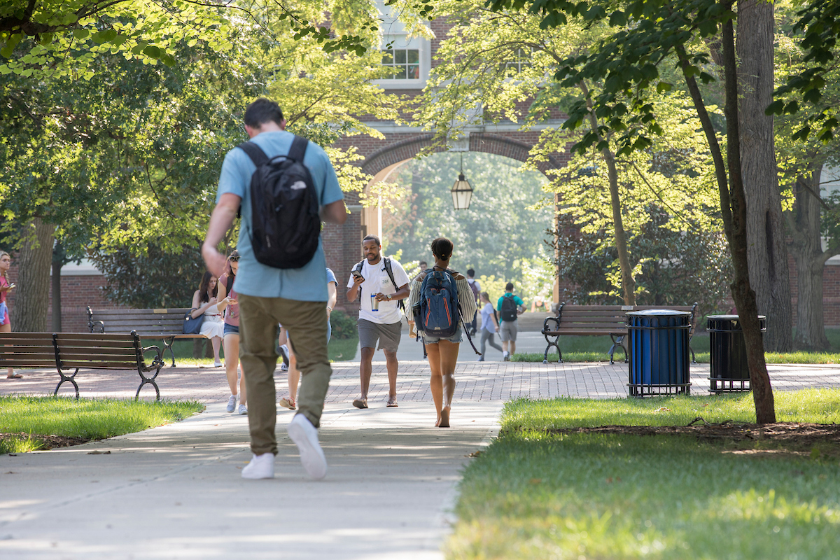 Students walk to class through the quad, with the arch visible in the background