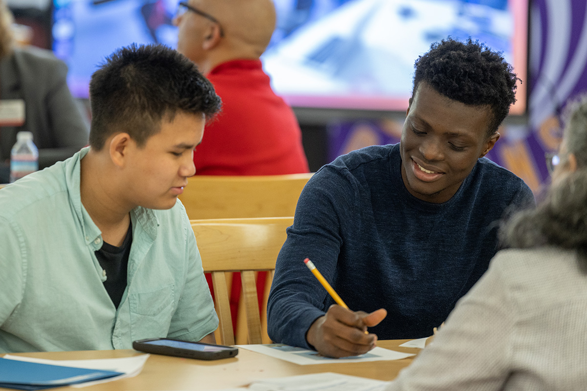 A student writes in a notebook while tutoring another student.