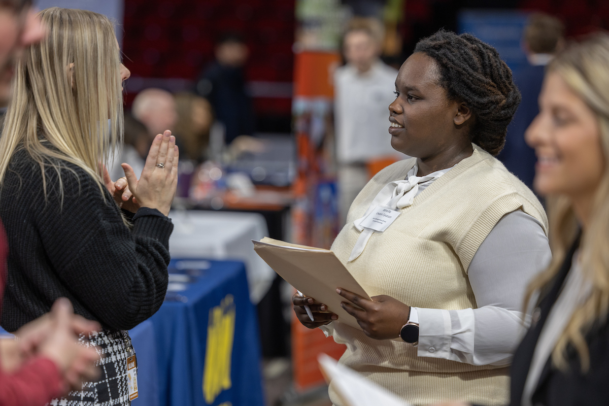 A student smiles while speaking with an employer at a Career Fair.