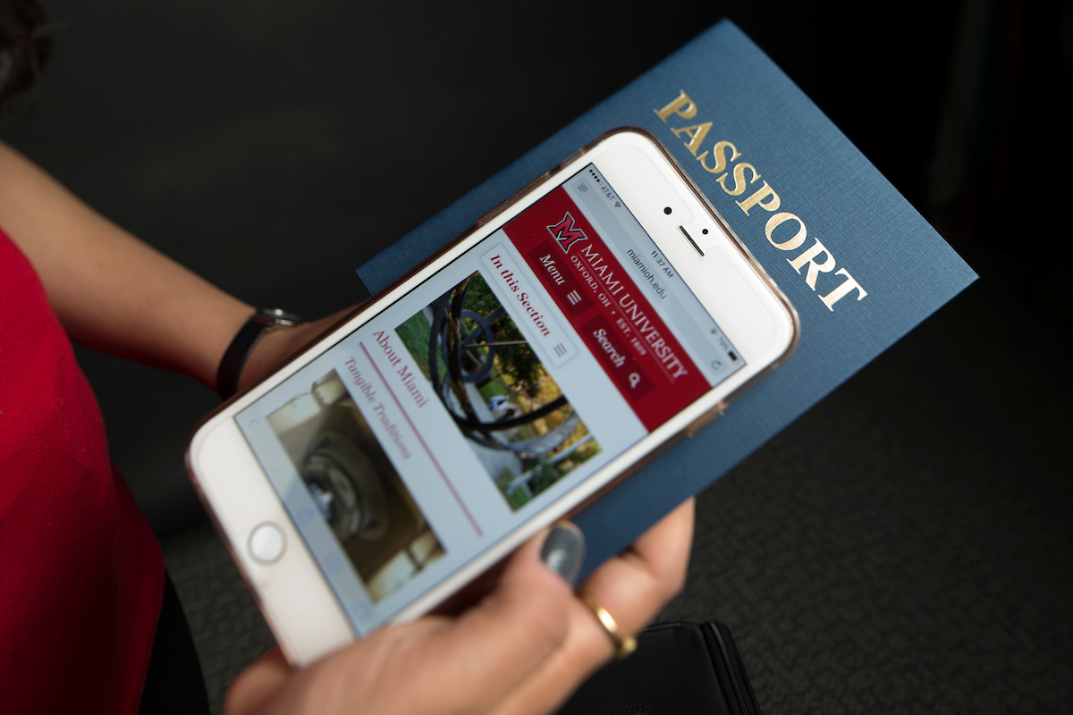 A student scrolls on a phone, which is sitting on a passport.