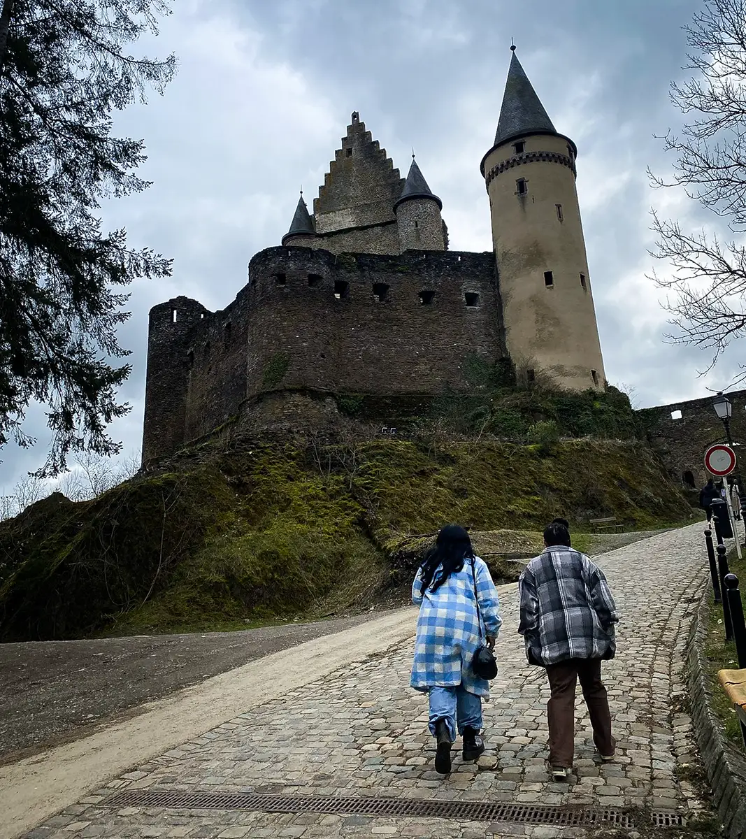 Two students walk toward a European castle on a stone path.