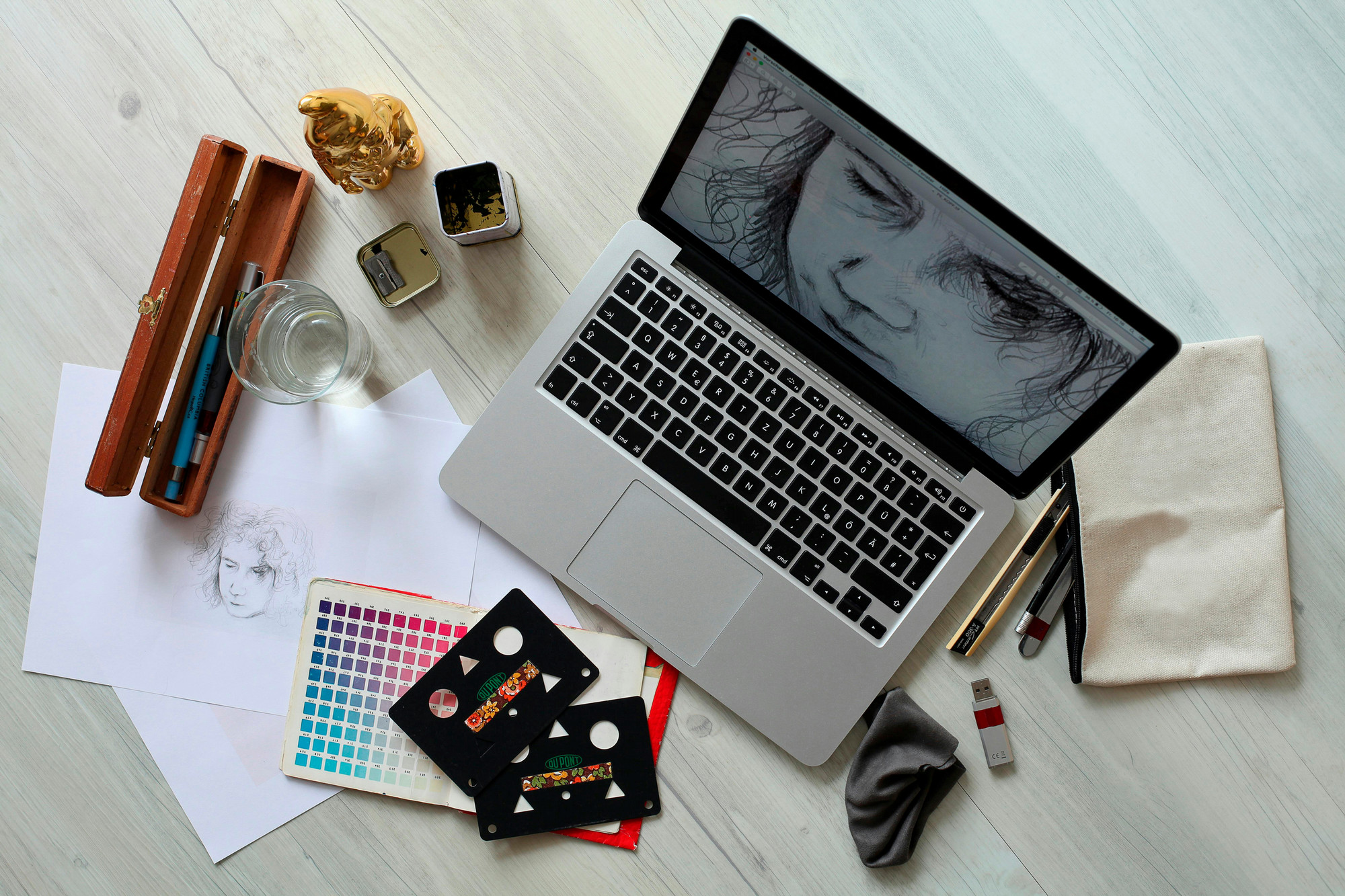 Art supplies and a sketch centered around a laptop displaying a picture of a woman.