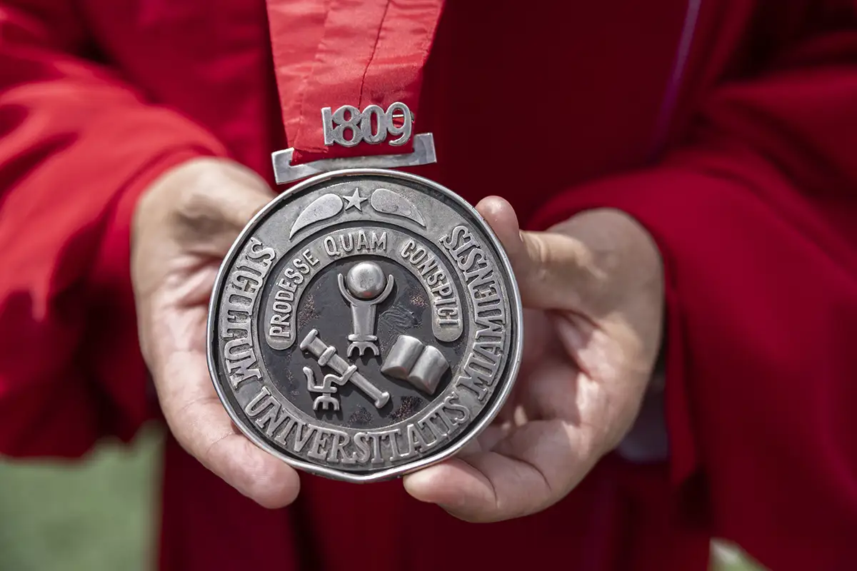 An alumni holds an 1809 medallion at graduation.