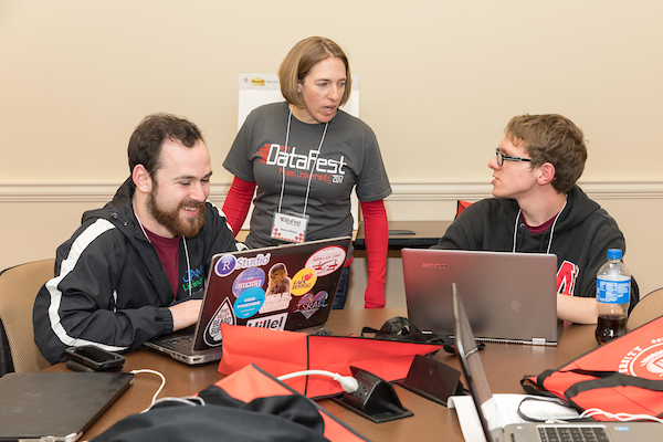 Three people surrounding two laptops having a discussion.