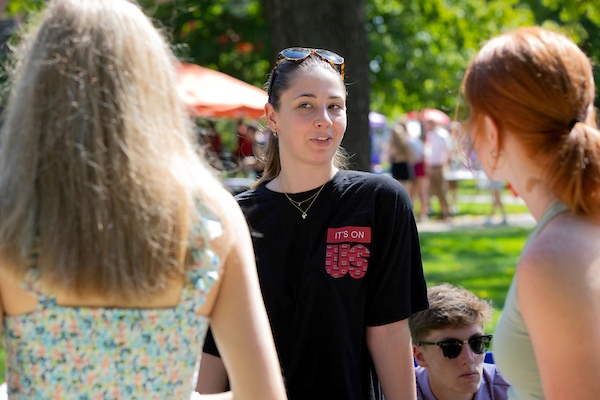 Student wearing an It's On Us tshirt at Mega Fair talking to two other students.