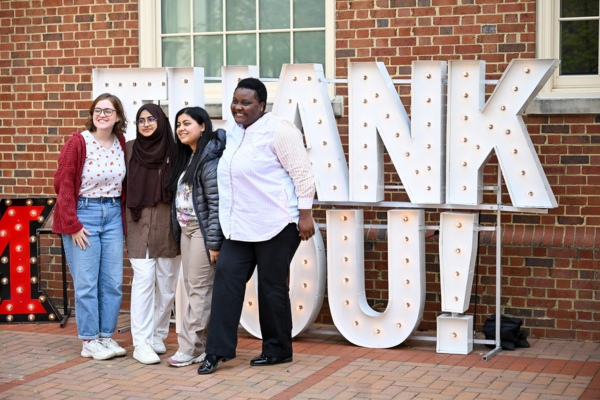 Four students posing in front of huge light up letters that spell thank you. 