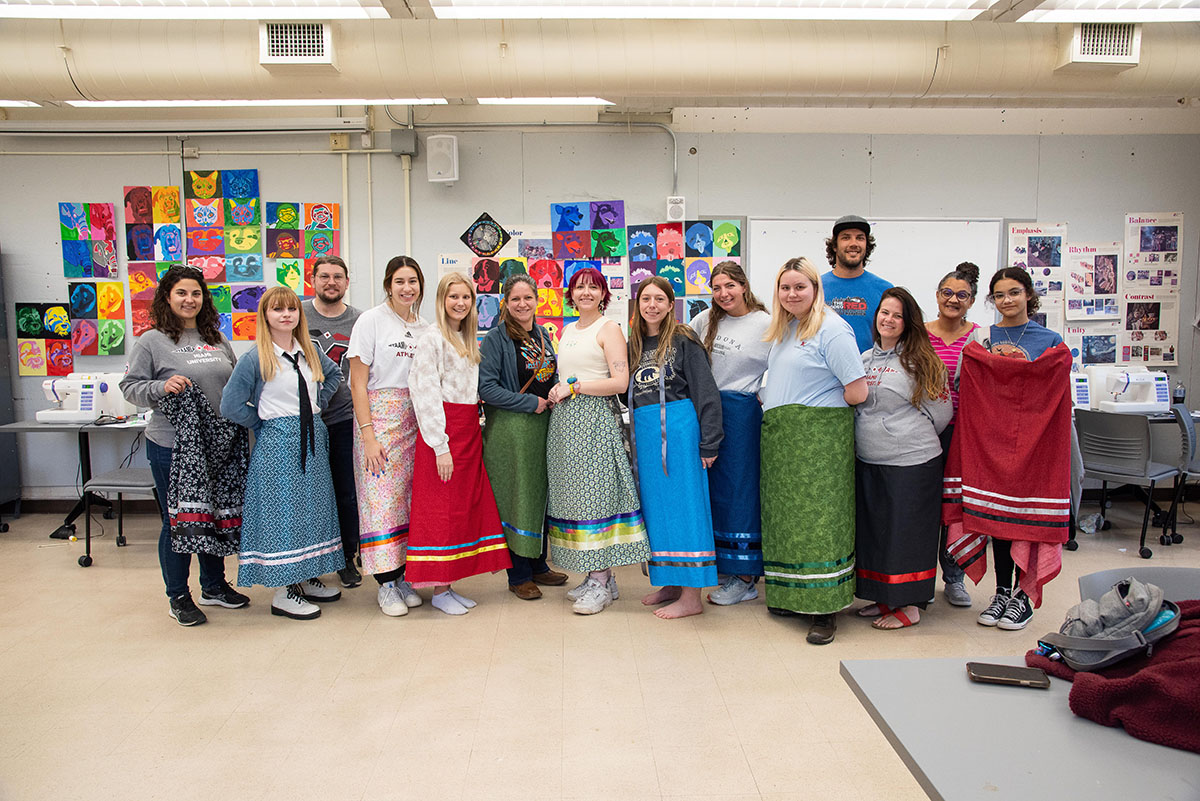 Miami students wearing colorful skirts and shawls decorated with myaamia ribbonwork. 