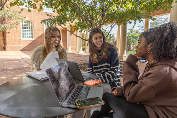 three femaie students sitting outside on their computers