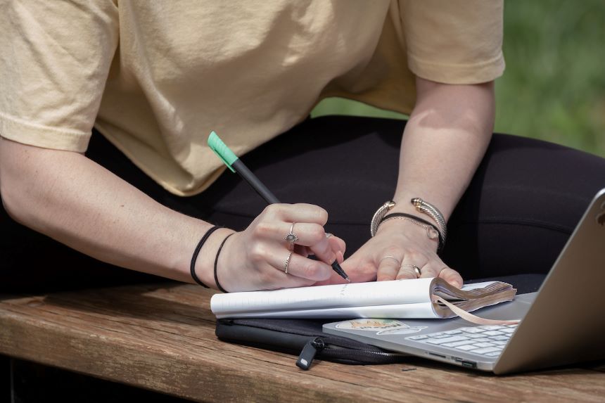 Person writing next to a laptop.