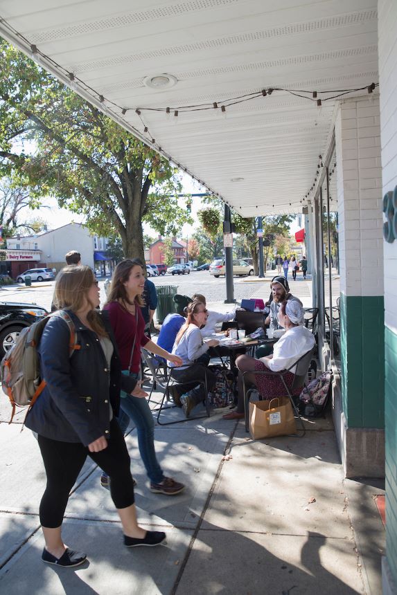 Students walk into a business while others sit at a table in the background.